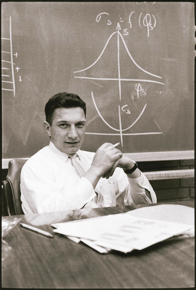 Black-and-white photo of Robert Noyce, seated at a desk in front of a chalkboard